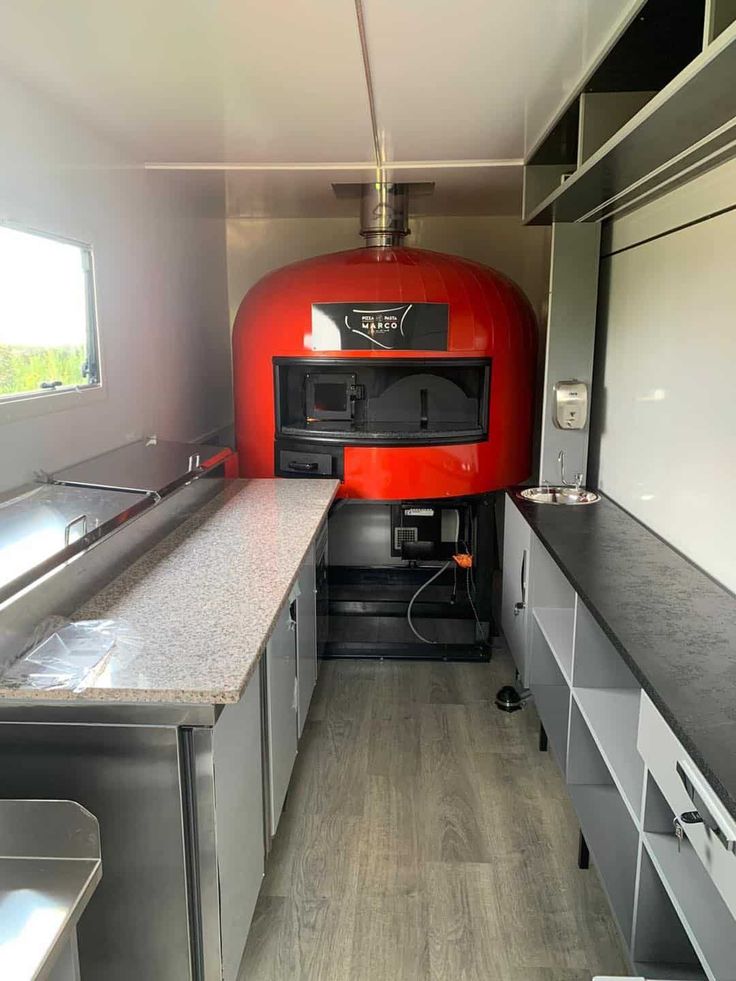 the inside of an rv with stainless steel cabinets and counter tops, including a red stove top oven