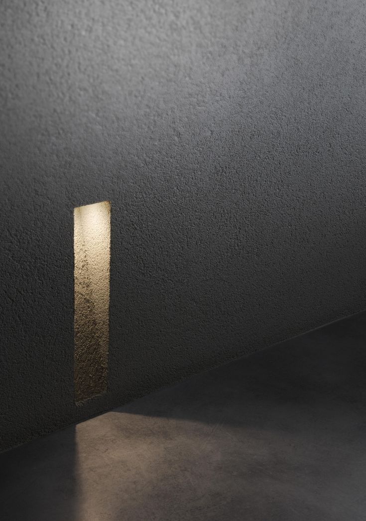 a light that is on in the middle of a room with dark walls and concrete flooring