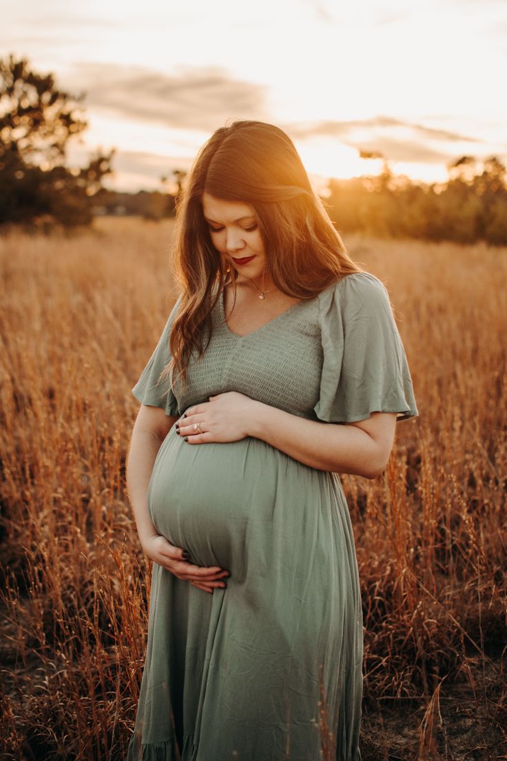 a pregnant woman standing in a field at sunset with her belly tucked under her stomach