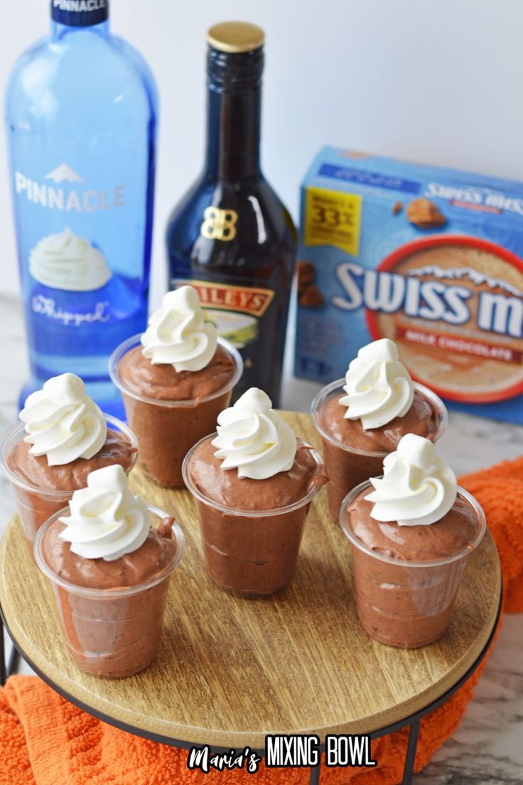 mini chocolate puddings with whipped cream on a wooden tray next to bottles of booze