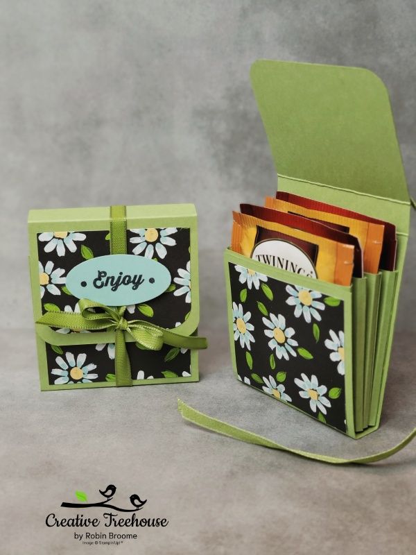 an open box with some cards in it and a green ribbon around the bottom that says enjoy