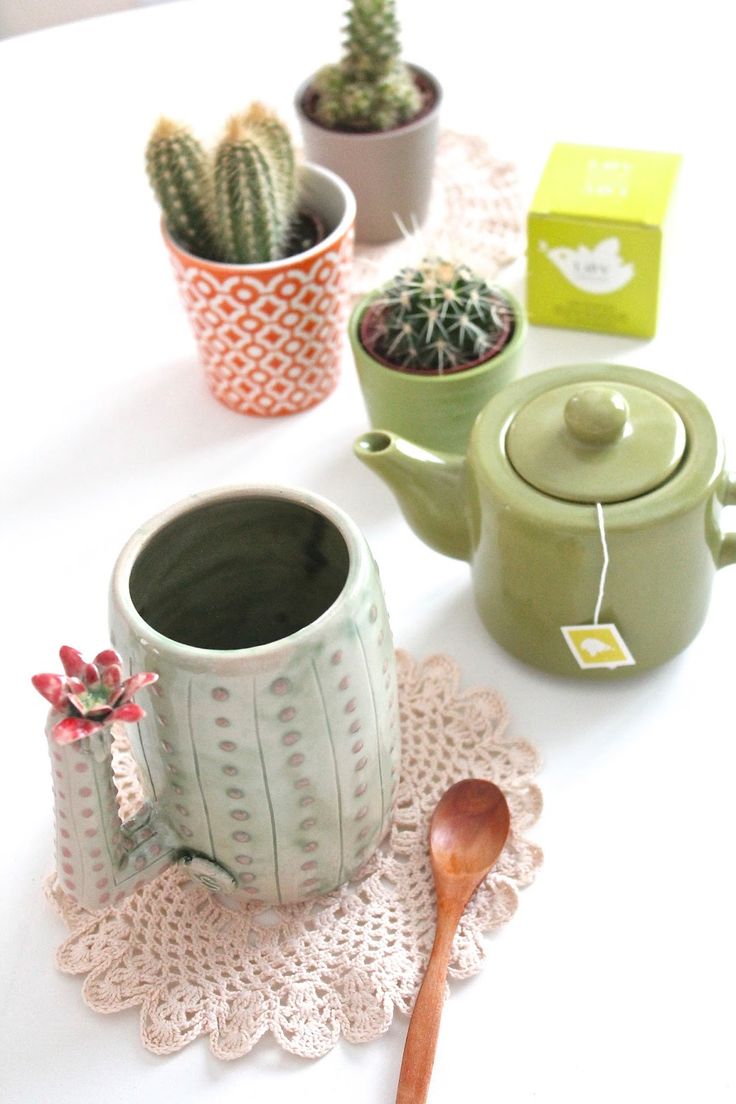 there is a tea pot with a wooden spoon on the table next to some cacti