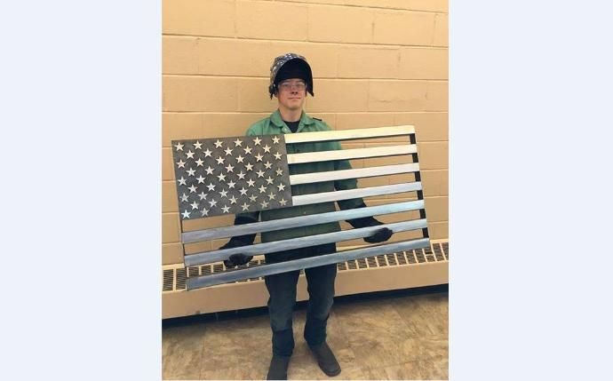 a person holding an american flag made out of metal bars and sticks in front of a wall