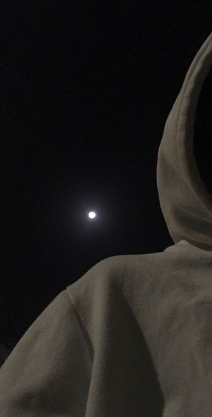 a person in a hooded jacket is looking at the moon