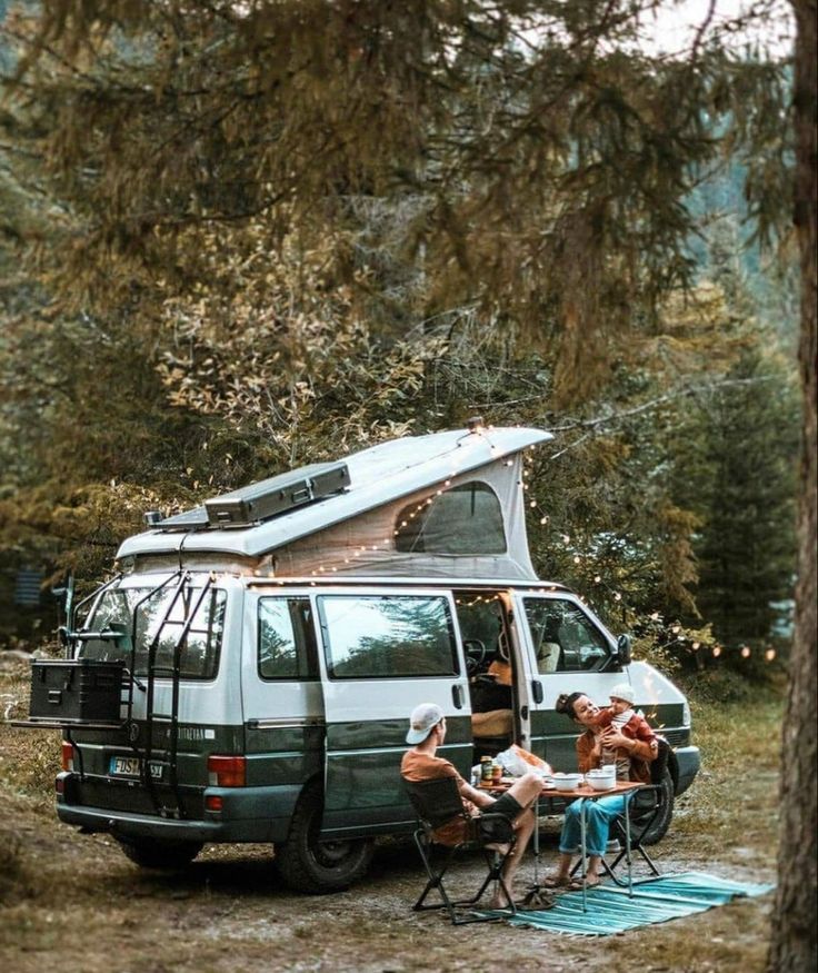 people sitting around a camper van in the woods