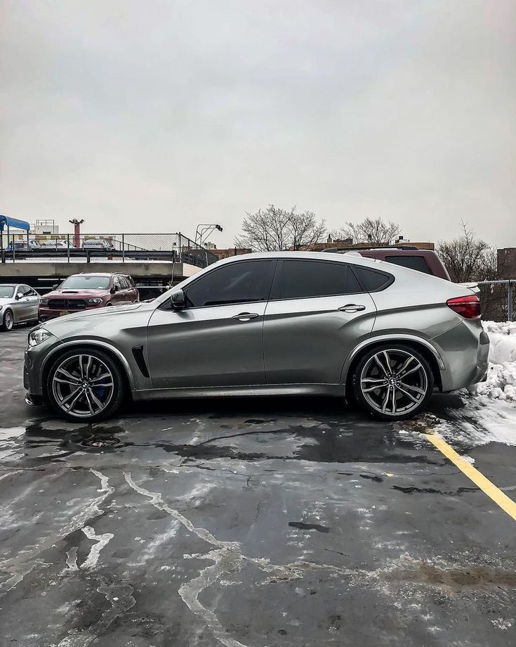 a silver car parked in a parking lot with snow on the ground and cars behind it