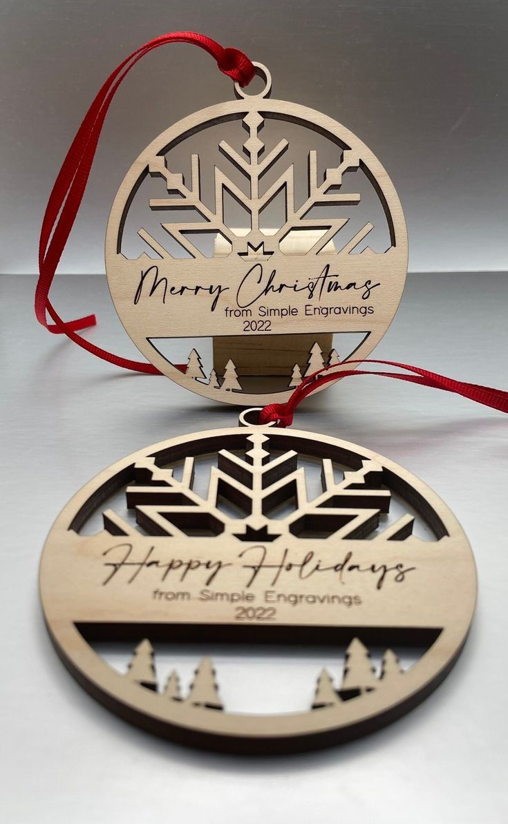 two wooden christmas ornaments with red ribbon on white table top, one has a snowflake ornament and the other says merry christmas