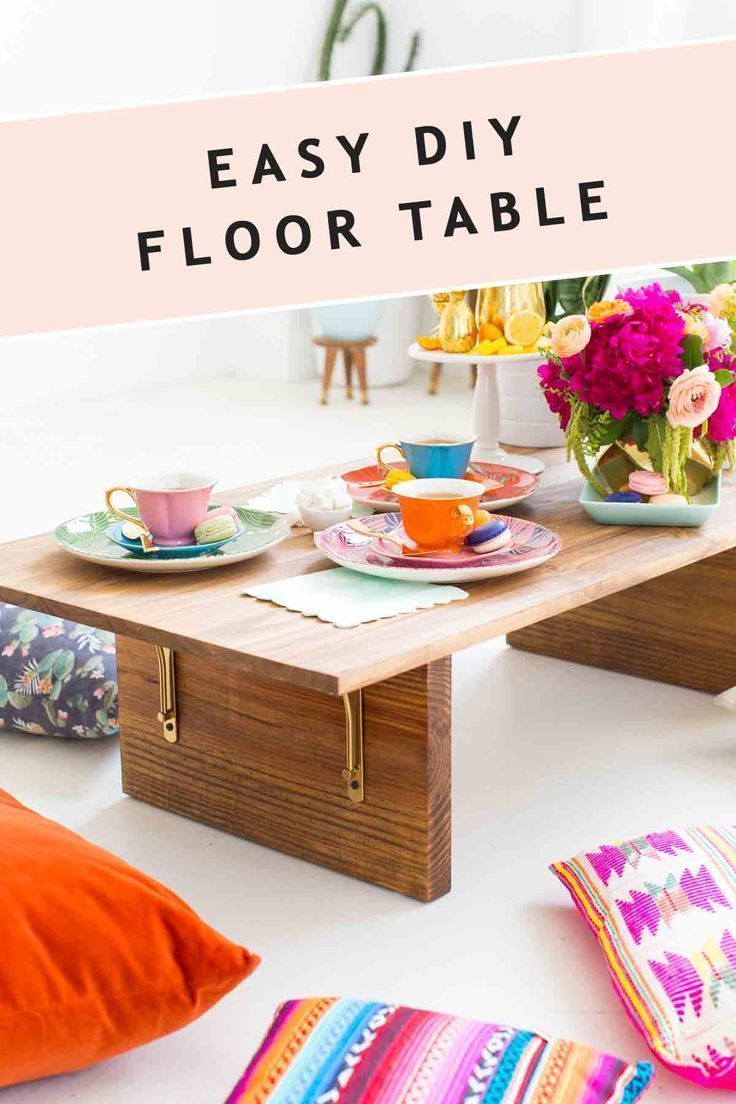 an easy diy floor table with plates and cups on it, surrounded by colorful pillows