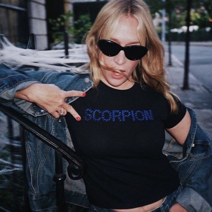 a woman with sunglasses pointing at the camera and wearing a scorpion shirt on her chest