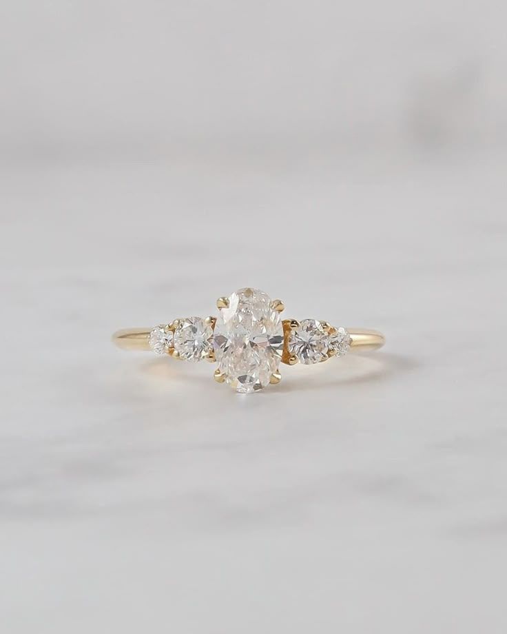 a three stone diamond ring on a white marble surface, with the top half in yellow gold