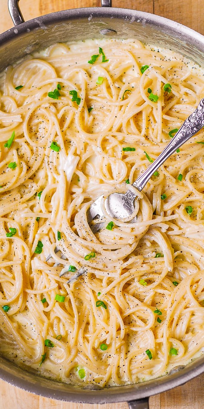 a pan filled with pasta and peas on top of a wooden table next to a silver spoon