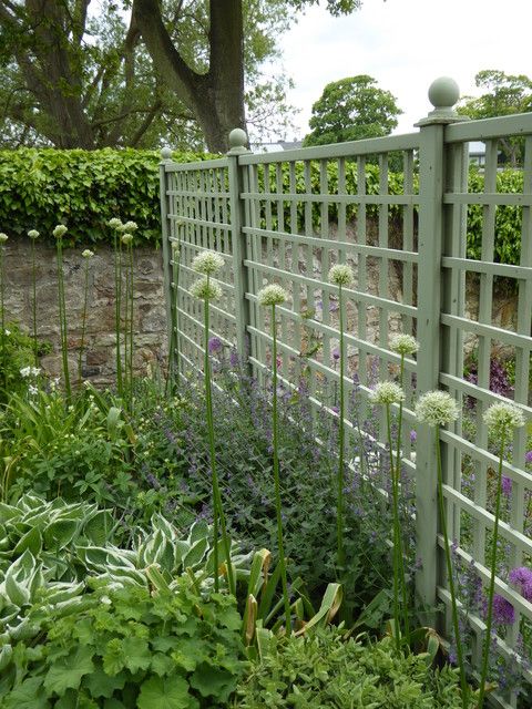 a garden filled with lots of flowers next to a green trellis fence and shrubbery