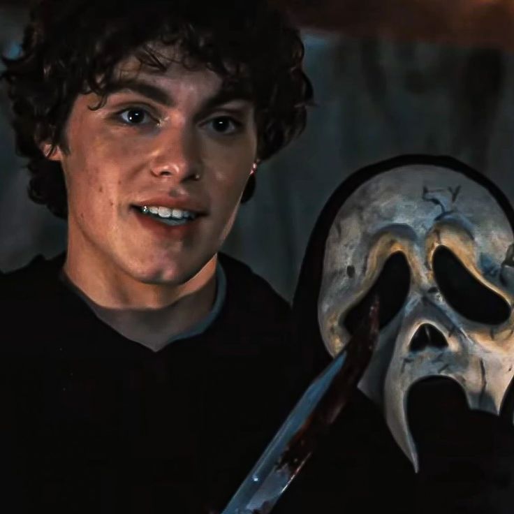 a young man holding a knife in front of a skull mask