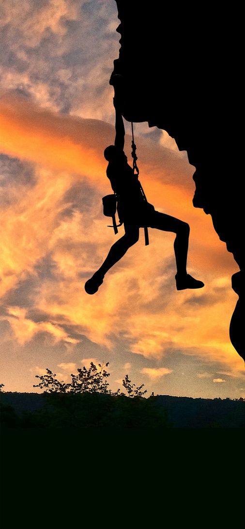 a man hanging off the side of a cliff while holding on to a rope as the sun sets