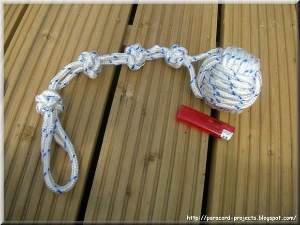 a ball of yarn tied to a rope on top of a wooden deck next to a crochet hook