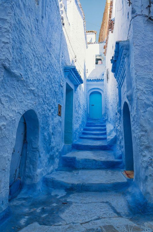 an alleyway with blue painted walls and steps leading up to the door in morocco