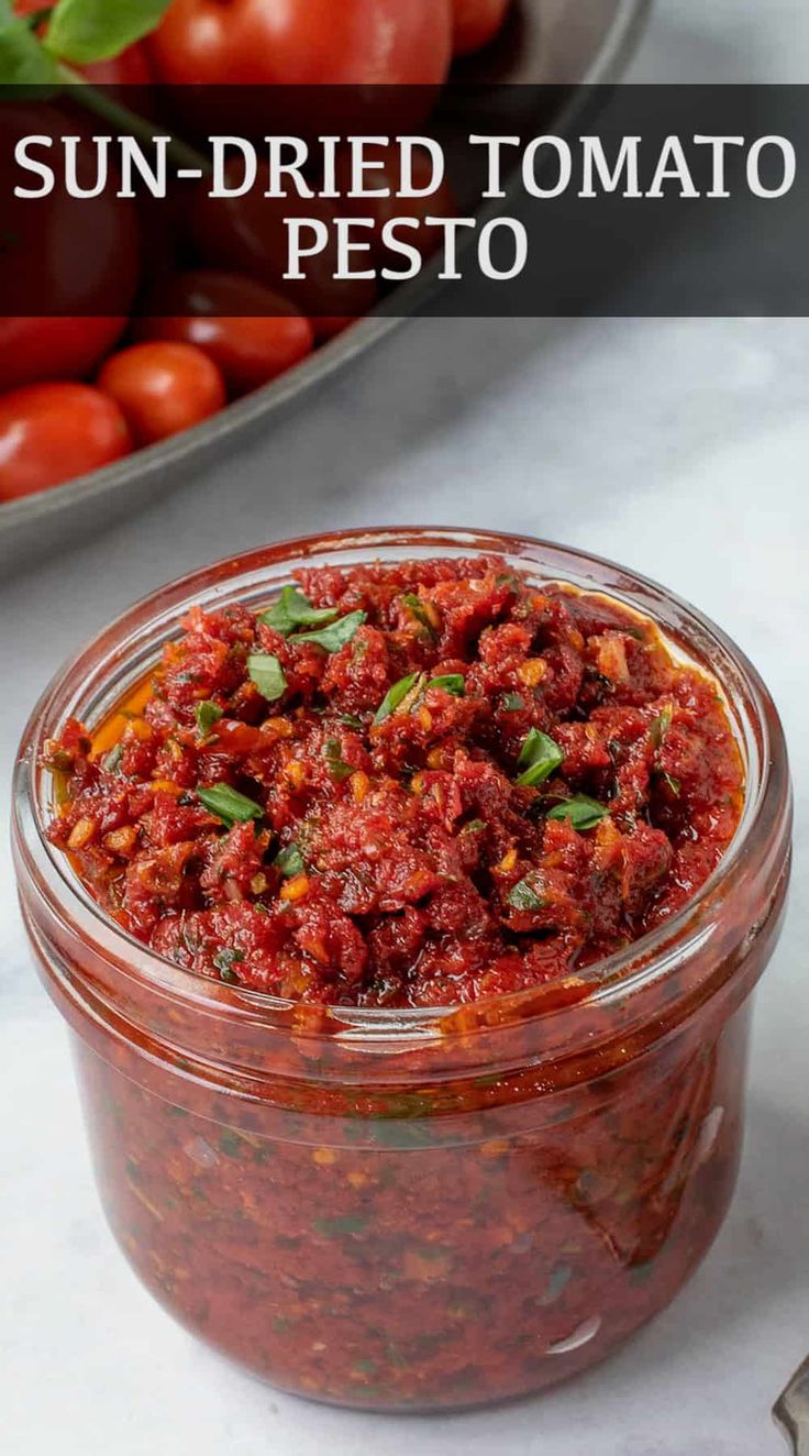 sun dried tomato pesto in a glass jar with tomatoes and basil on the side