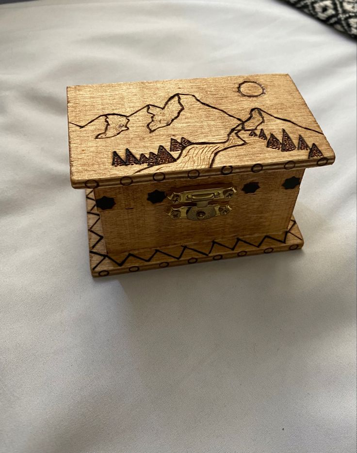 a wooden box sitting on top of a bed with mountains drawn on the side of it