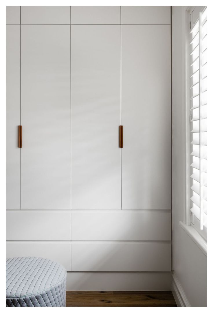 a bedroom with white cupboards and wooden flooring, along with a round ottoman in the foreground