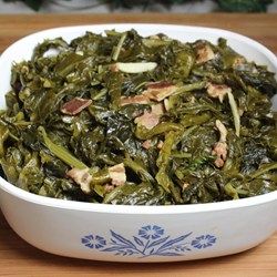 a white bowl filled with cooked greens on top of a wooden table next to an orange