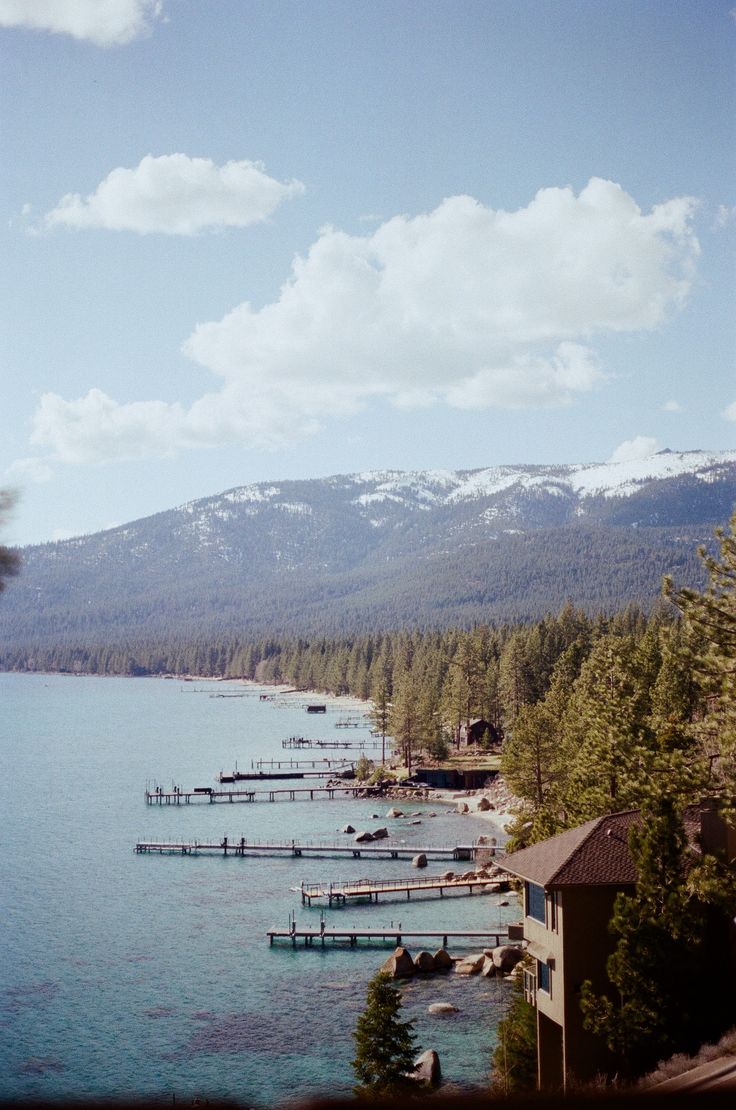 boats are docked in the water next to some trees and snow covered mountain range behind them