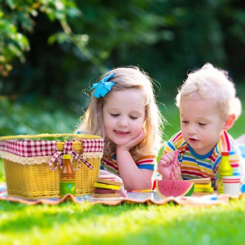 two young children laying on the grass with picnic items in hand and looking at each other