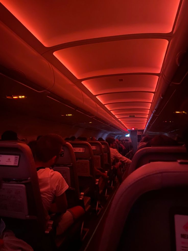 the inside of an airplane with red lights and people sitting in seats on either side