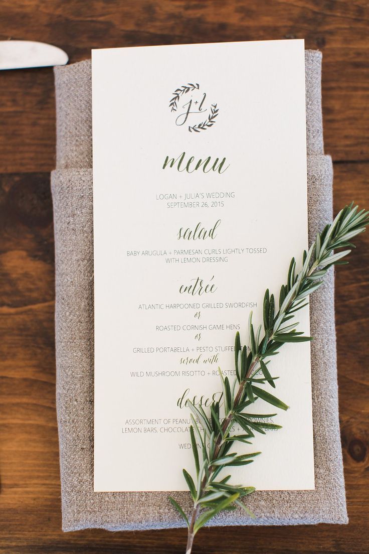 an elegant menu with greenery is displayed on a napkin and place setting for the guests to sit at