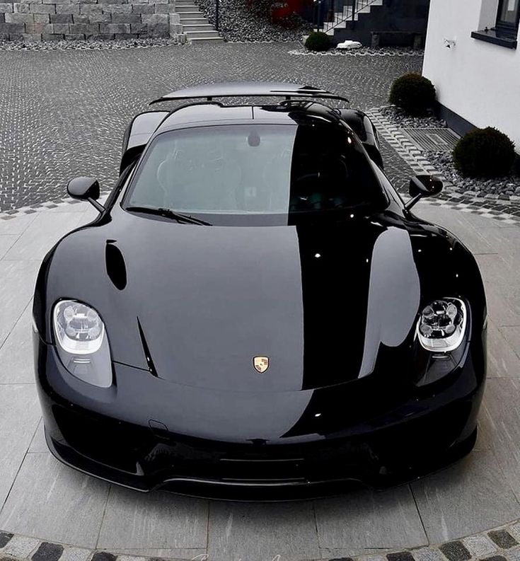 a black sports car parked in front of a white building on a cobblestone driveway