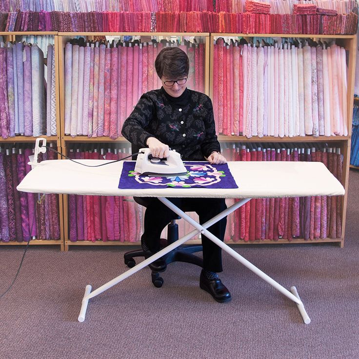 a woman ironing fabric on an ironing board in front of a bookcase