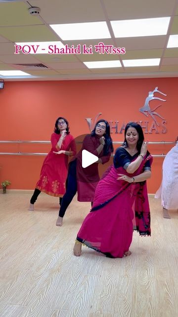 three women in pink dresses are dancing on a wooden floor with an orange wall behind them