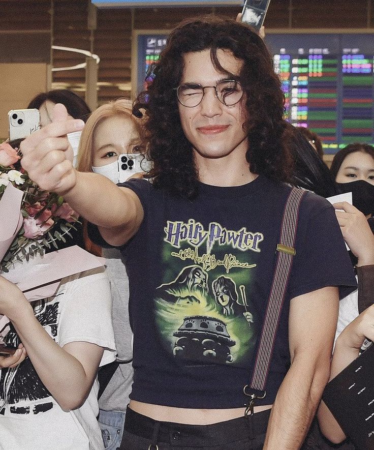 a man with long hair and glasses taking a selfie in front of a group of people