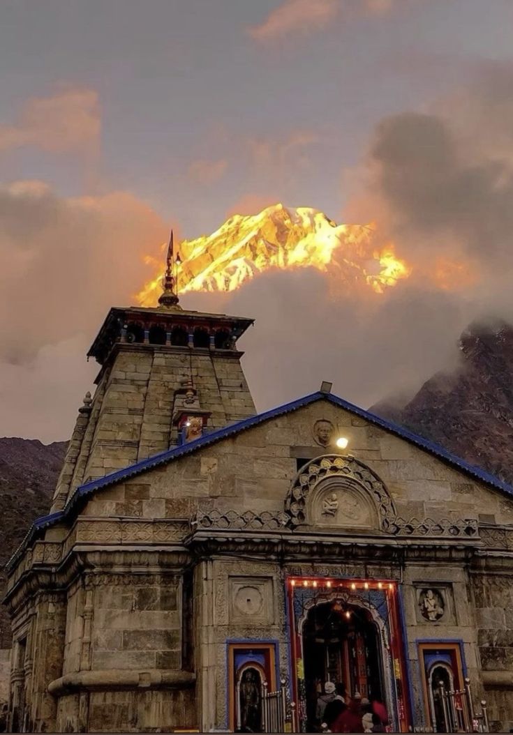 an old building with a fire coming out of it's roof and mountains in the background