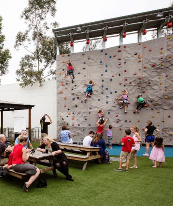 people are sitting at picnic tables in front of a climbing wall with children on it