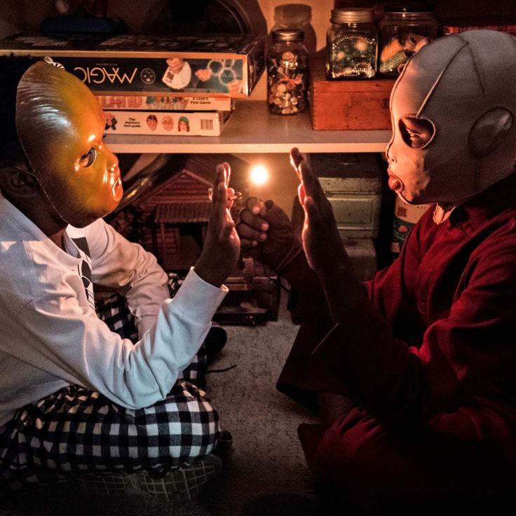 two children wearing masks sitting on the floor in front of a table with books and candles