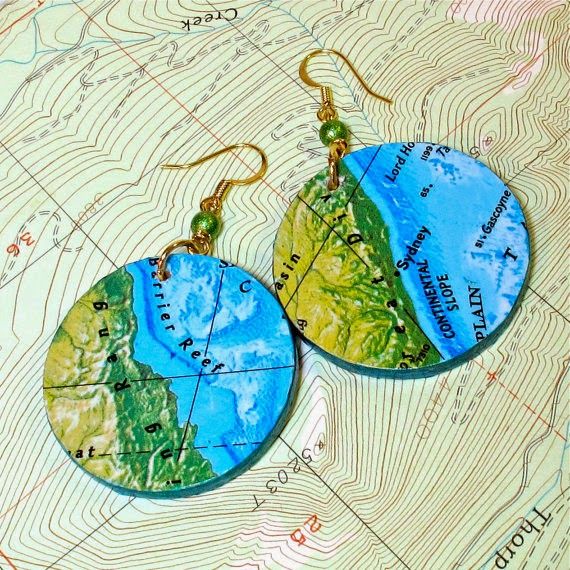 two blue and green earrings with the names of different countries on them, sitting on top of a map