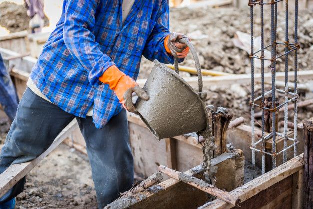 a man pouring cement into a bucket on top of a construction site with other men in the background