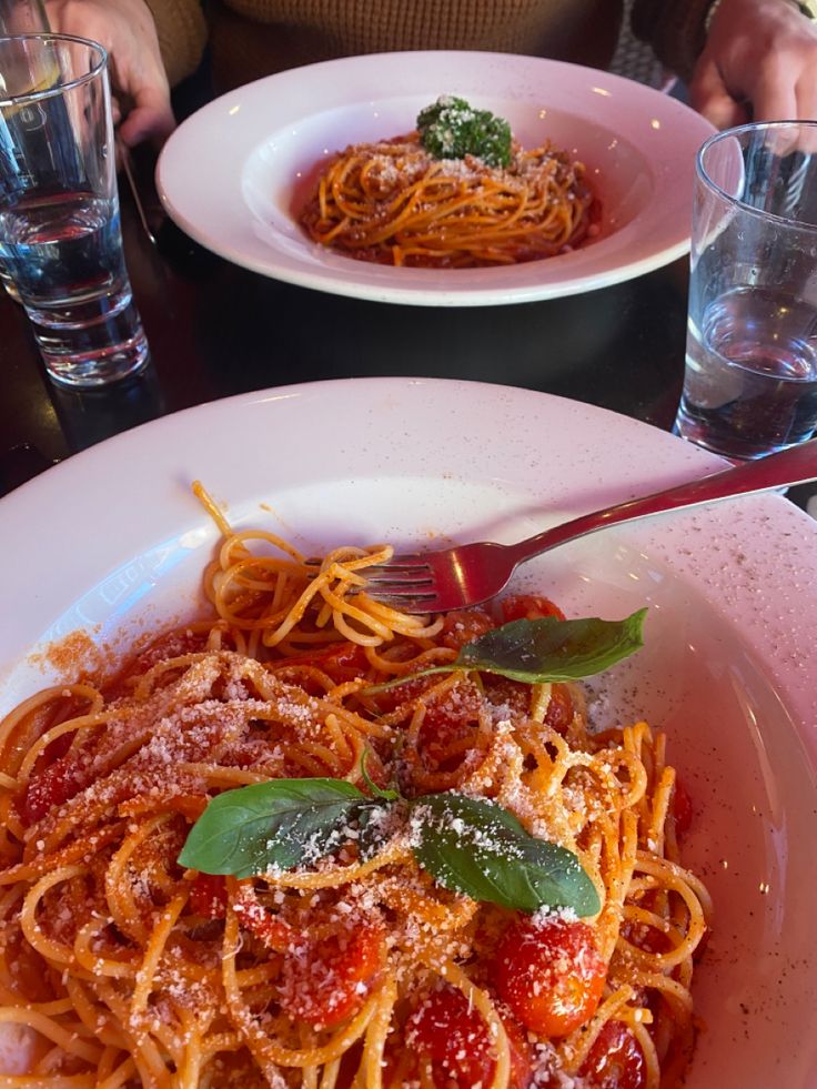 two plates of spaghetti with tomato sauce and parmesan cheese on the side at a restaurant