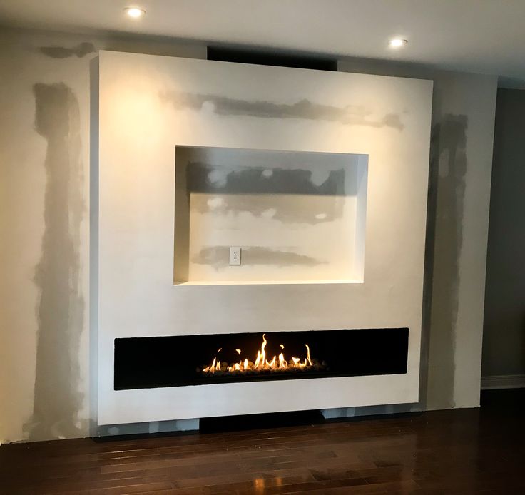 a fire place in the middle of a room with white walls and wood flooring