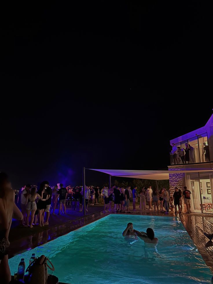 people are gathered around the pool at night