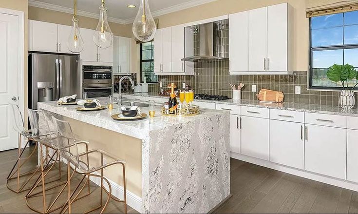 a large kitchen with marble counter tops and white cabinets, along with two bar stools