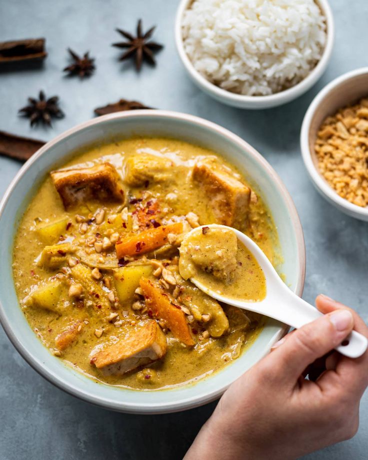 a person holding a spoon in a bowl filled with curry and rice next to other bowls