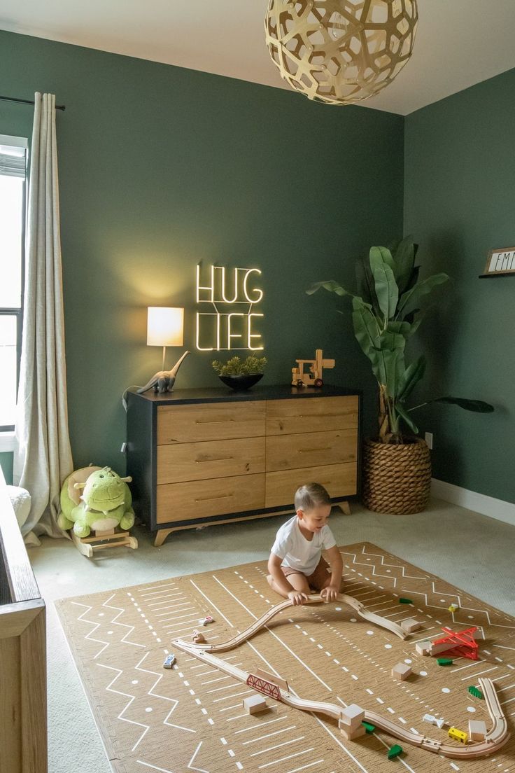 a toddler plays with his toy train set in the corner of a room that's painted green