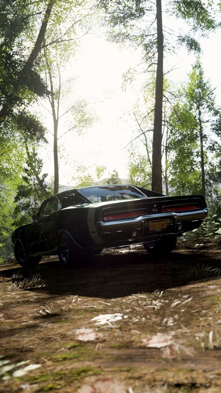 an old muscle car parked in the woods on a dirt road with trees around it