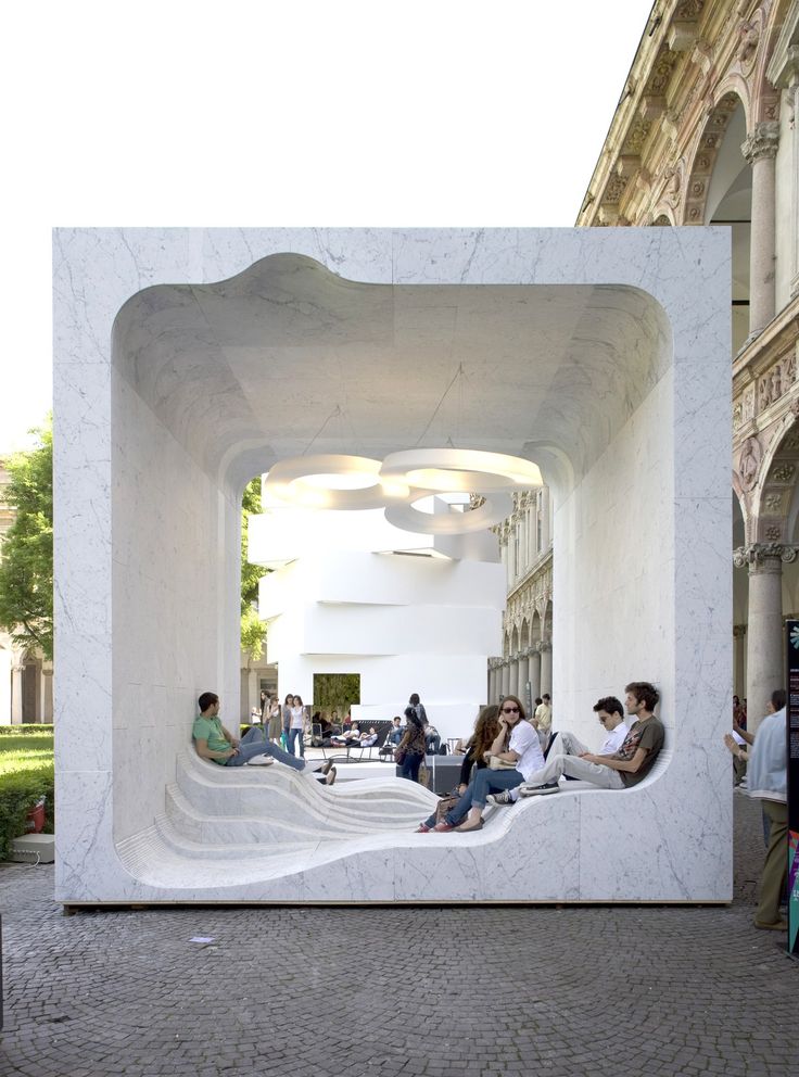 people are sitting on benches in the middle of a building with white walls and columns