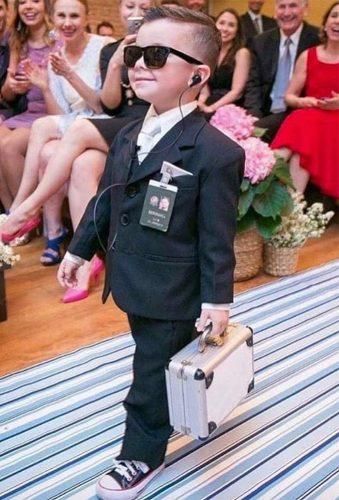 a young boy dressed in a suit and sunglasses with headphones, carrying a suitcase