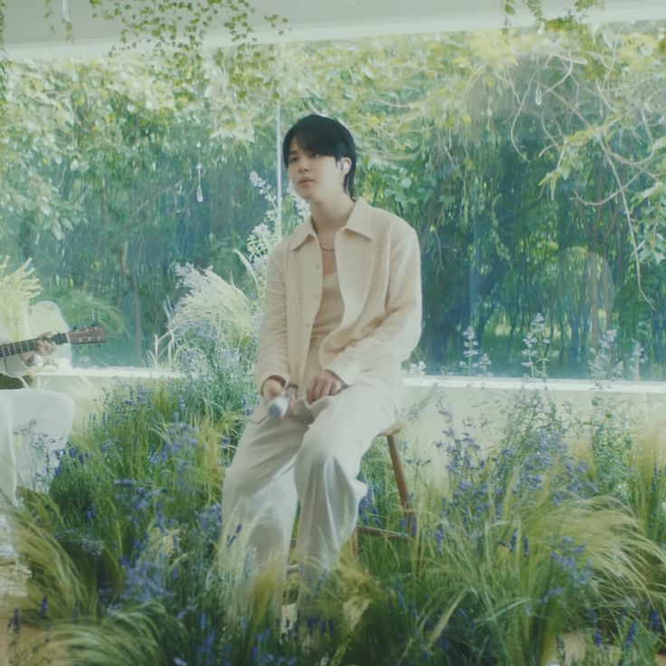 a man sitting on top of a chair next to a forest filled with green plants