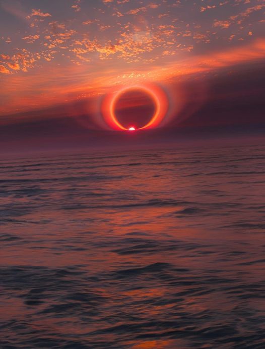 an eclipse is seen in the sky over the ocean at sunset, with red and orange clouds