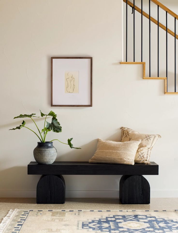 a black bench sitting under a stair case next to a potted plant on top of a rug