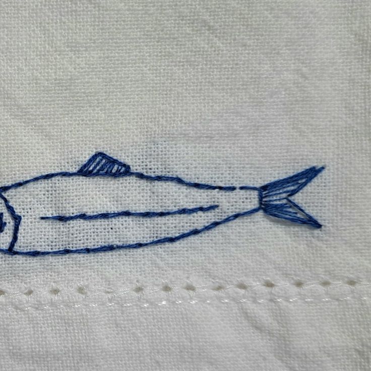 embroidered fish on white linen with stitching in blue and white thread, closeup